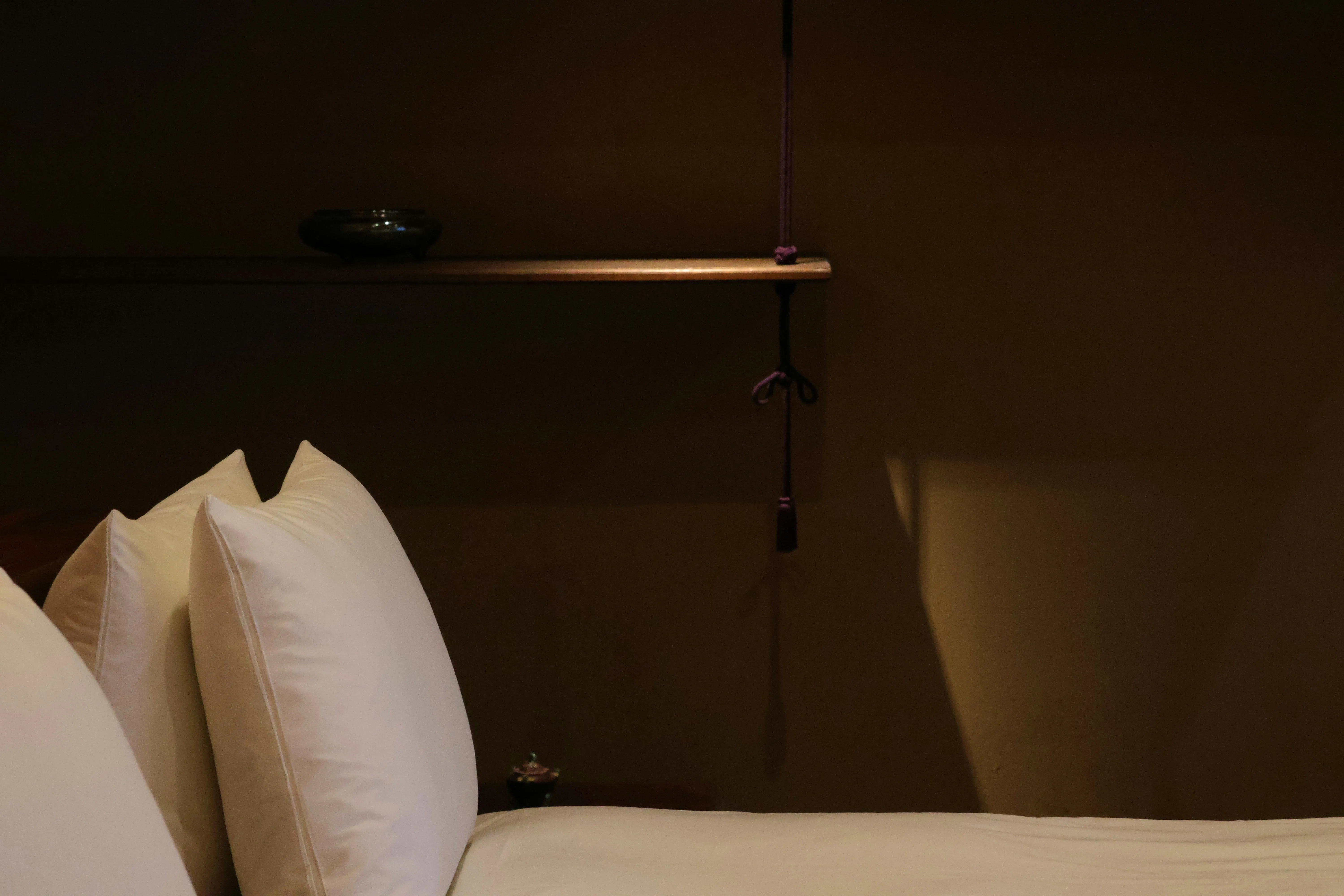 En minimalistisk nyredd hotellseng med hvite hotellputer i et rom med nedstemt belysning.